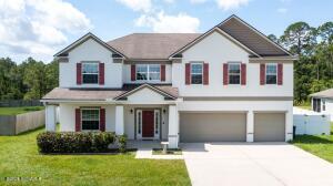 Two-story traditional luxury home at 118 Walnut Way in Kingsland, GA — off-white stucco siding with burgundy shutters and front door, a covered front porch, an attached three-car garage, and a manicured lawn framed by pine trees