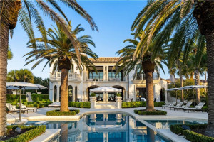 Mediterranean-style oceanfront villa at 106 East 18th Street on Sea Island, GA — white stucco exterior with arched architecture, viewed across a multi-section swimming pool framed by palm trees and manicured landscaping