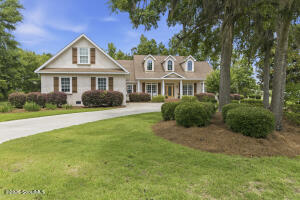 Traditional off-white brick home at 106 Majestic Drive in Brunswick, GA — one-and-a-half-story residence with three gabled dormers, a columned front portico, tan-shingled roof, and mature trees with Spanish moss on a manicured lawn in a gated community