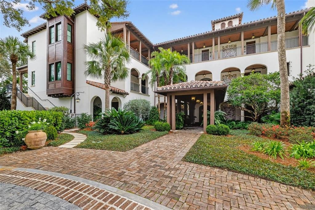 Ocean Forest penthouse at 100 Ocean Road #F on Sea Island, GA — Mediterranean-style estate with white stucco walls, terracotta barrel-tile roofs, dark-wood bay windows and arched loggia overlooking a brick-paved courtyard with palm trees