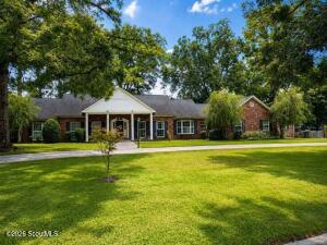Single-story ranch-style home at 207 Plantation Drive in Waycross, GA — red-brown brick exterior with a white columned front portico, a bay window, and a manicured lawn framed by mature trees on a sunny day